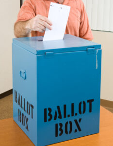 Closeup of a man's hand placing his ballot in the box.