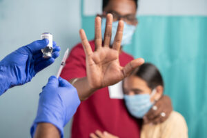 Selective focus on coronavirus vaccination bottle - Concept of Parents vaccine hesitancy for children, showing by saying no or stop gesture to vaccine with hand at hospital Selective focus on coronavirus vaccination bottle - Concept of Parents vaccine hesitancy for children, showing by saying no or stop gesture to vaccine with hand at hospital