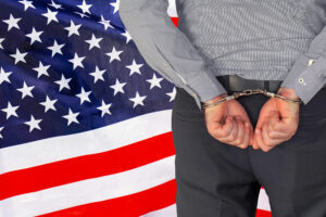 Male with handcuffs on the background of the USA flag. Back view. Concept of prisons and corruption in US Male with handcuffs on the background of the USA flag. Back view. Concept of prisons and corruption in US