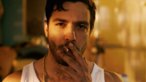 Smoking Brutal Gang Member with Gold Chain Looks into Camera with Defiance. Underground Drug Laboratory is in Background. Smoking Brutal Gang Member with Gold Chain Looks into Camera with Defiance. Underground Drug Laboratory is in Background.